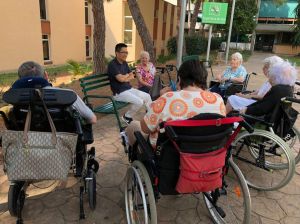 Gruppo di signore in sedia a rotelle in circolo intorno a un padre camilliano