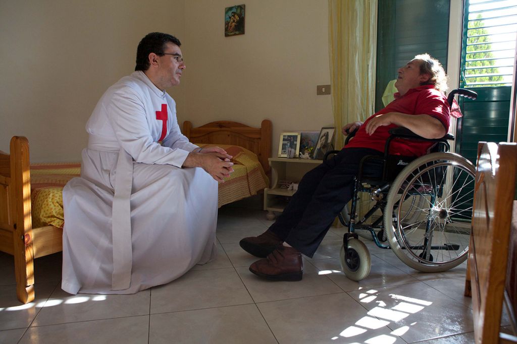 fratello camilliano conforta un malato in sedia a rotelle